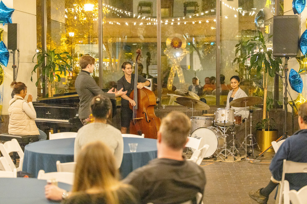 Audience members listen to jazz music in a glass-walled courtyard