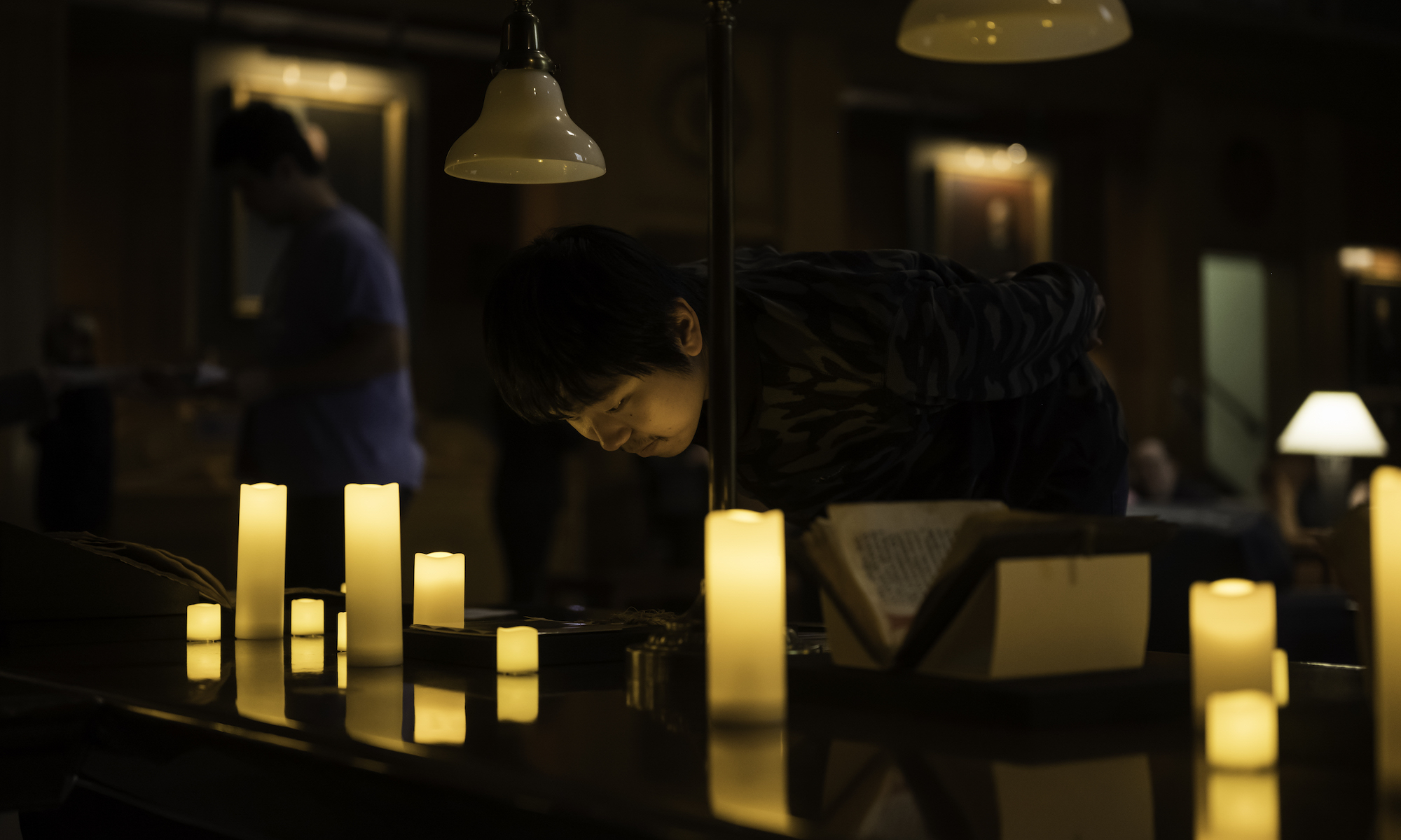 A person looks over an old manuscript in a room lit only by electric candles