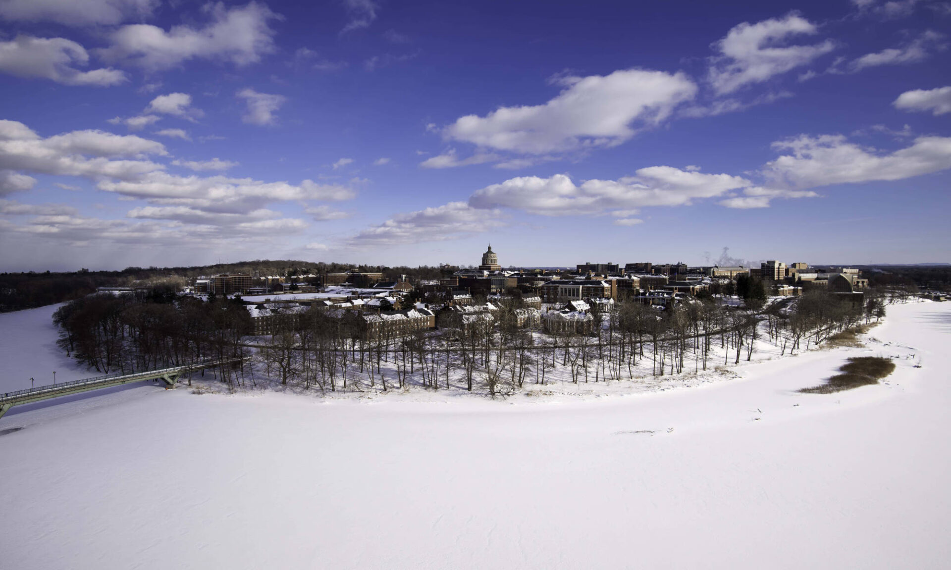 Snow-covered River Campus and Genesee River with blue skies and white clouds overhead.