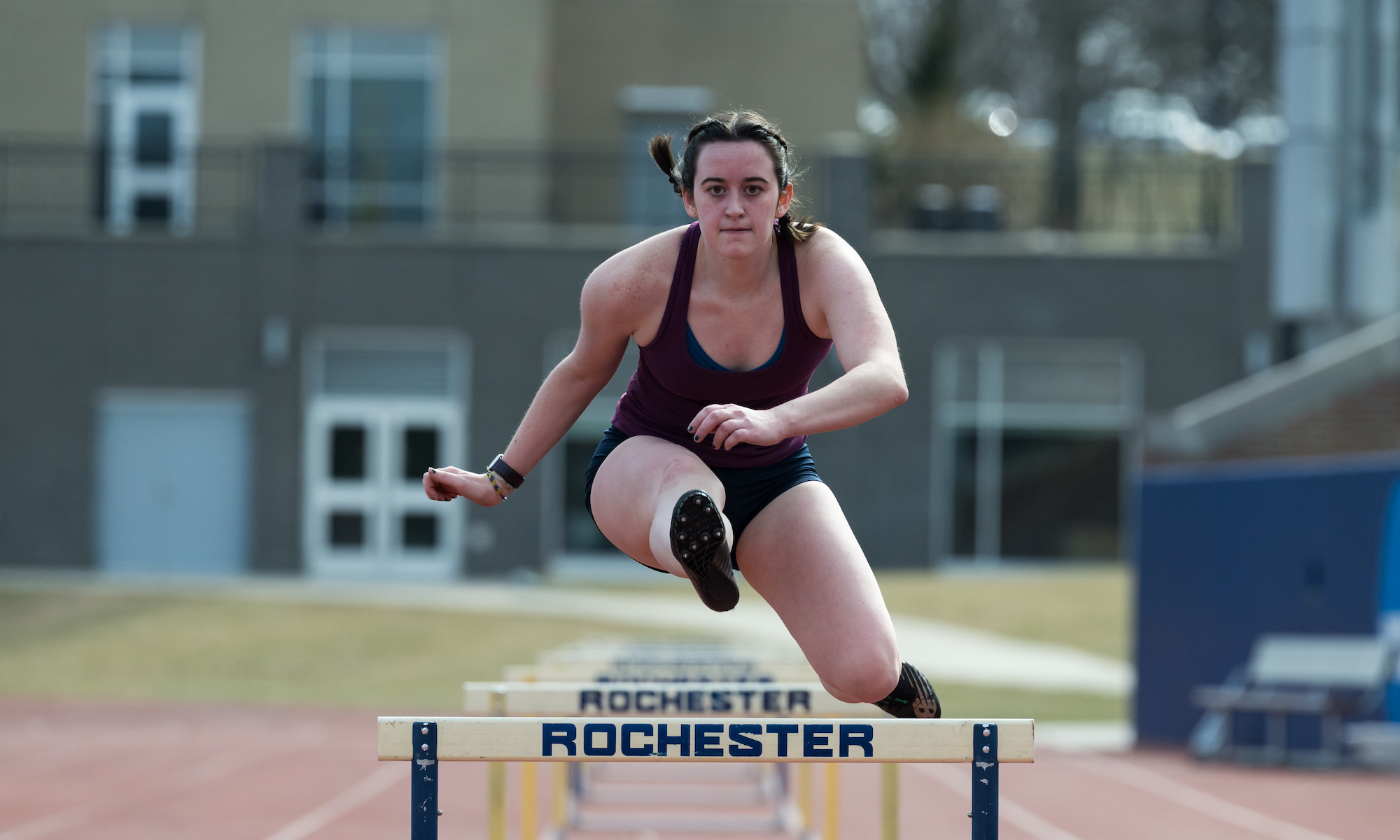 Female hurdler jumps over a Rochester-branded hurdle