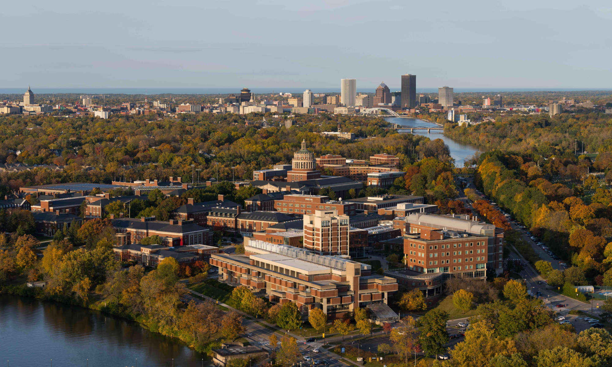 Aerial view of the University of Rochester's River Campus with the City of Rochester skyline in the background and a sliver of the Genesee River in the bottom left corner.