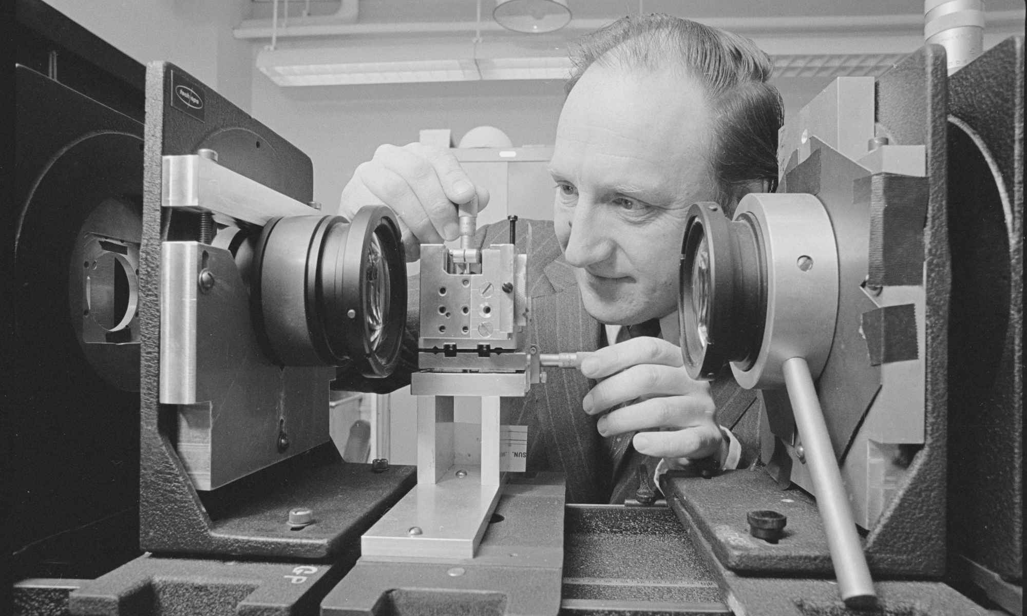 Feature image Black-and-white photo of Brian J. Thompson working with an optical setup.