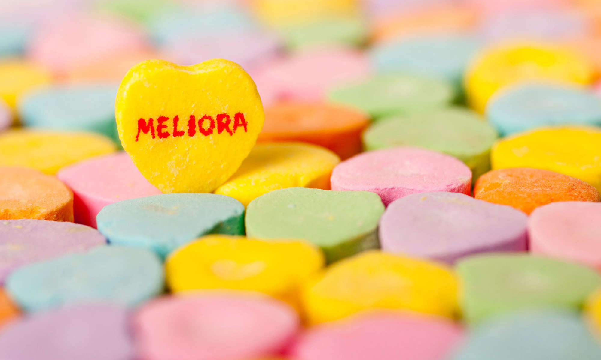 Candy hearts laid flat but a yellow one with "Meliora" written on it is upright.