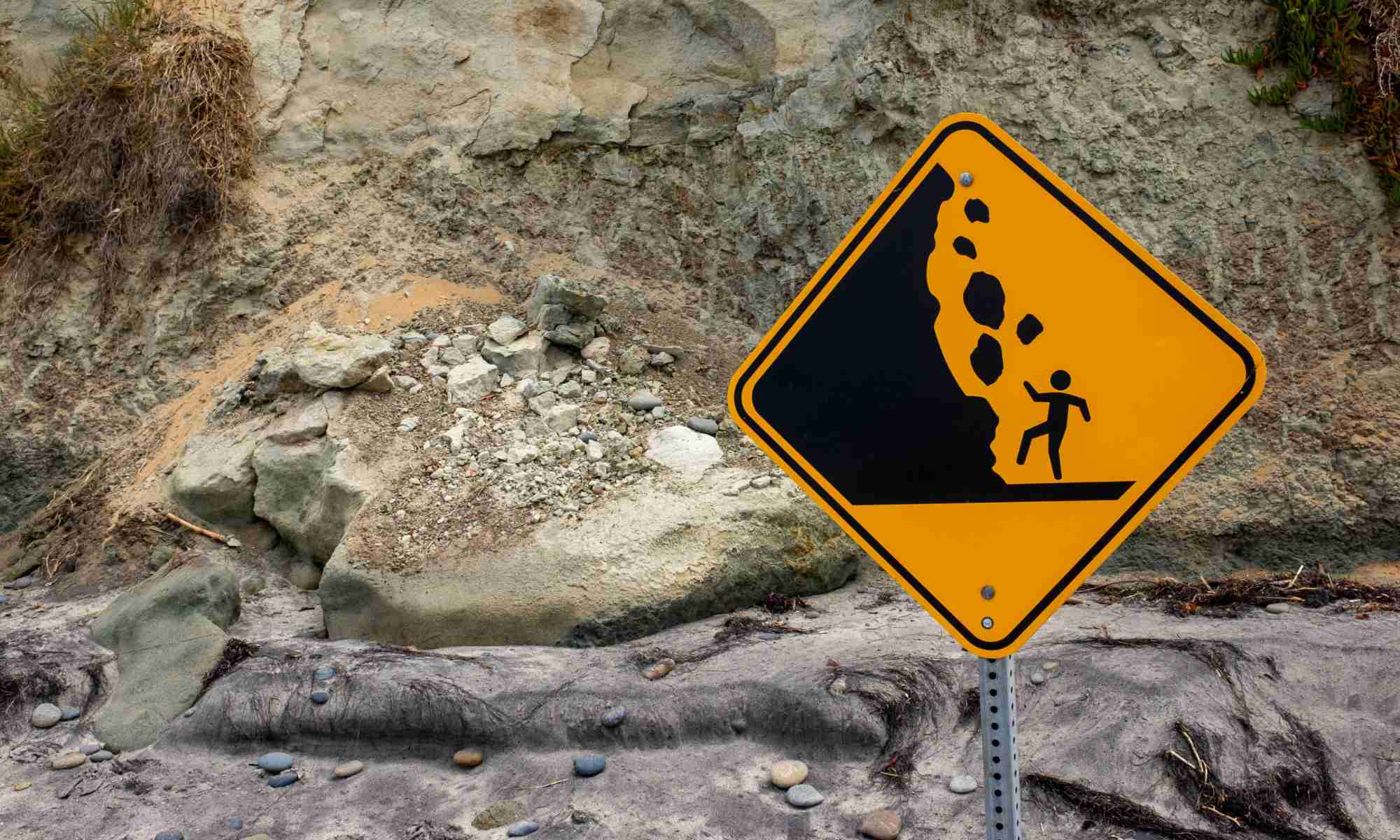 Feature image Falling rocks warning sign in front of rocks and boulders of various sizes along a mountainside to illustrate the idea of granular systems.