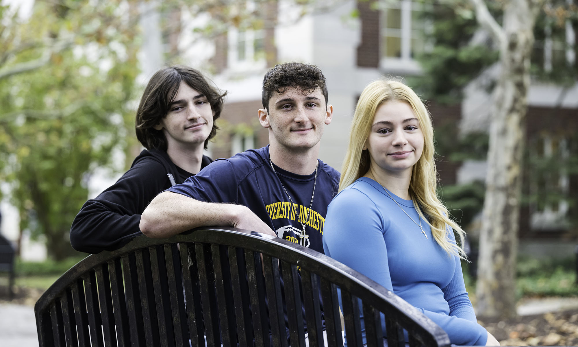 three students seated on a bench look over the back of the bench.