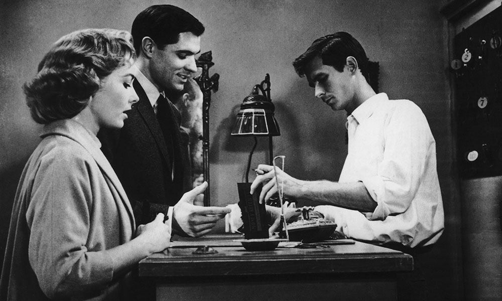Still from Psycho horror film showing Norman Bates greeting Marion Crane and Sam Loomis at hotel desk.
