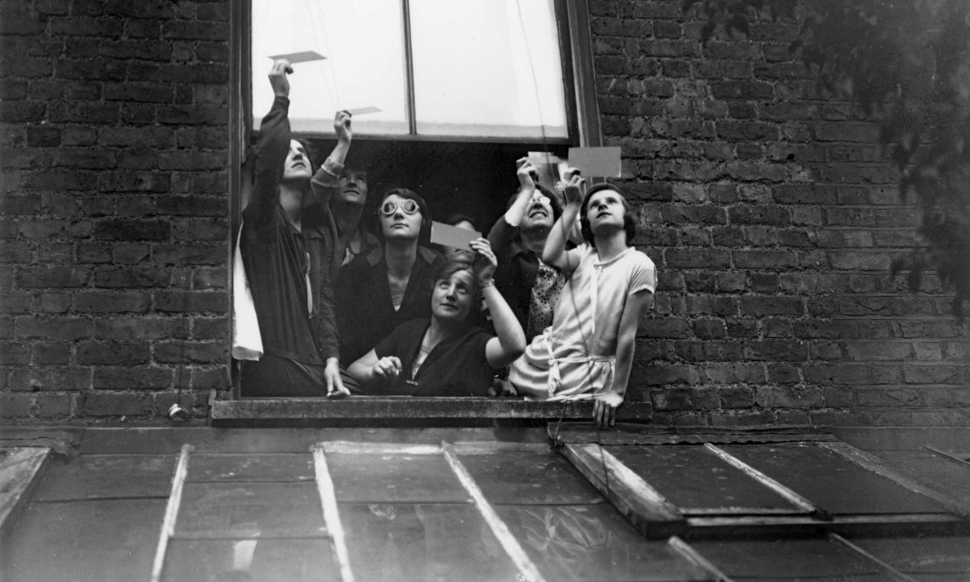 A group gathered in a window to view the total solar eclipse through smoked glass.