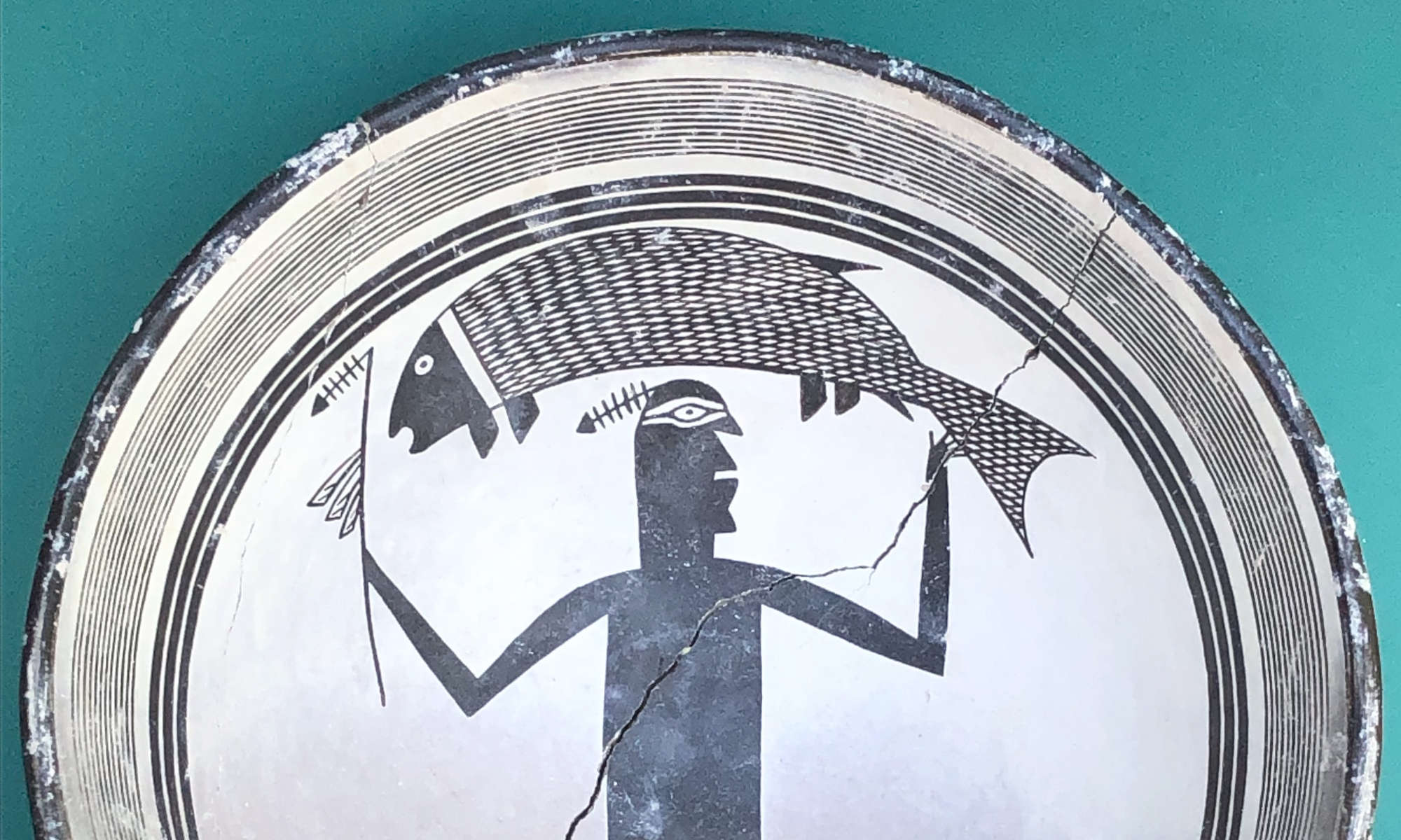 Close-up of a Native American art replica Mimbres bowl featuring a geometric figure holding a fish aloft.