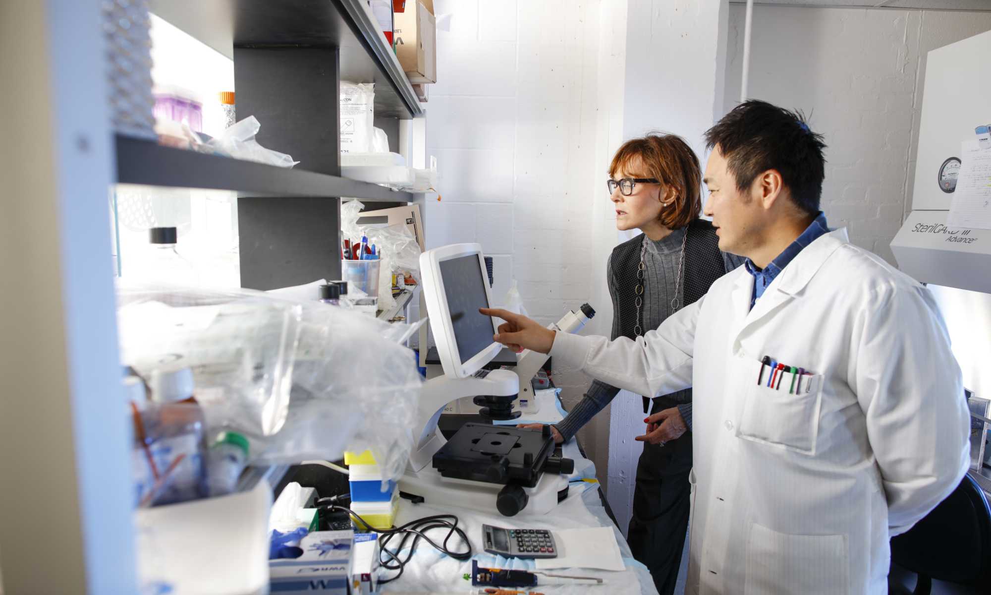 Two RNA research scientists in a lab analyzing the results of an experiment on a computer monitor.