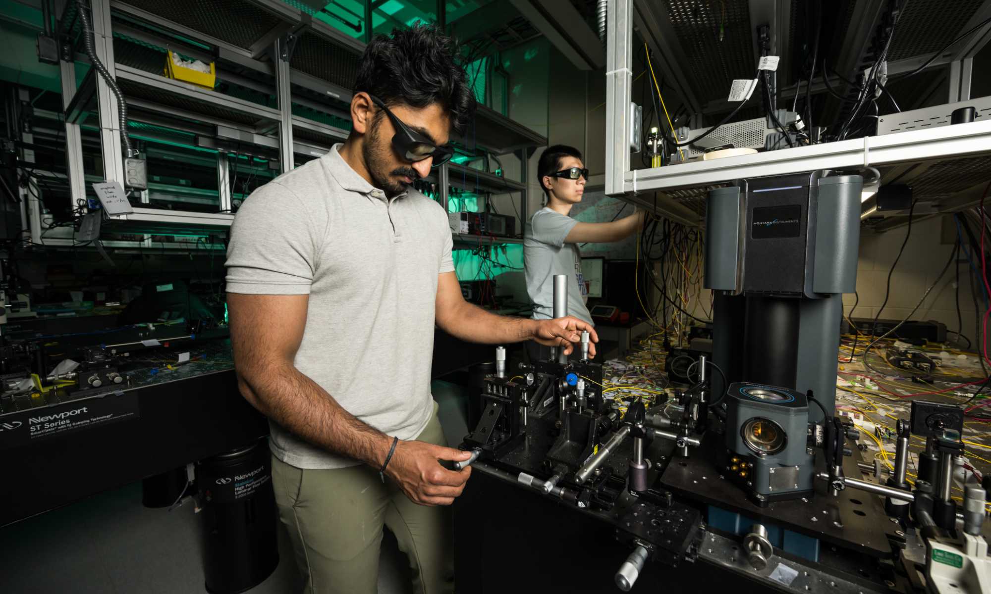 Two researchers wearing protective eyewear manipulate the equipment in an optics lab to produce surface acoustic waves.