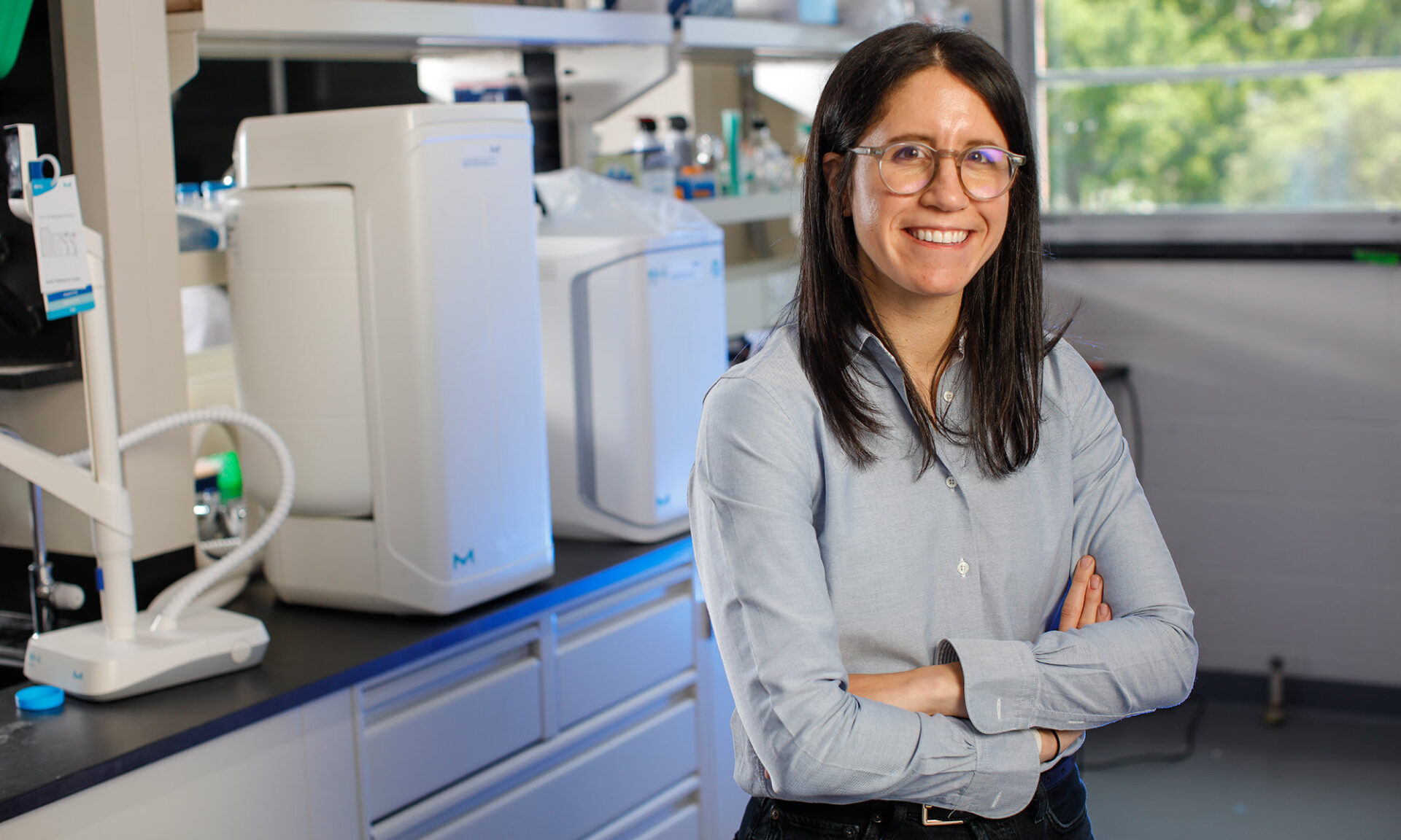 Allison Lopatkin stands with her hands crossed in front of some lab equipment.