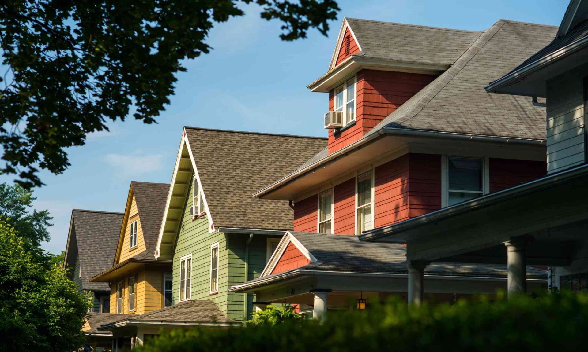 The upper halves of about five Rochester, New York, houses framed by green trees and shrubs and a blue sky to illustrate the University of Rochester's expanded home ownership incentive program.