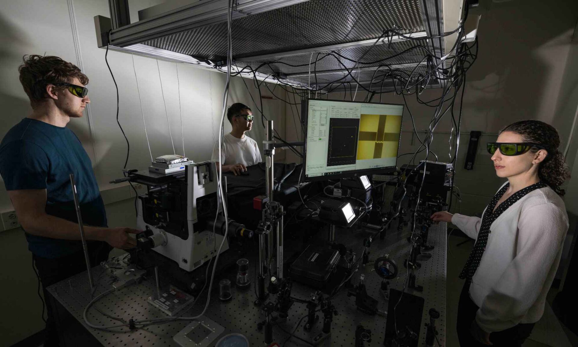 Three people wearing protective eye gear in a lab demonstrate heat transfer mapping techniques that are displayed on a computer screen.