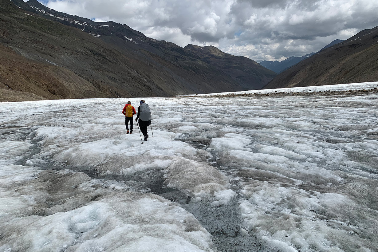 Two hikers walk off into the distance along a glacier.