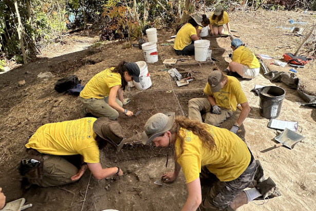 Eight University of Rochester undergraduate students in yellow shirts conduct an archaeological excavation.