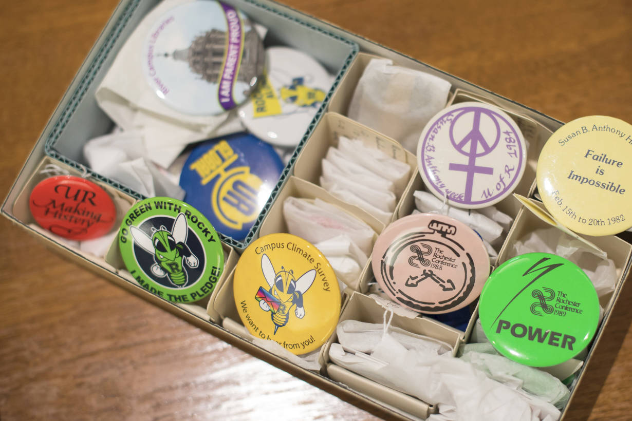 A box filled with University of Rochester pins, badges, and other historical and archival paraphernalia.