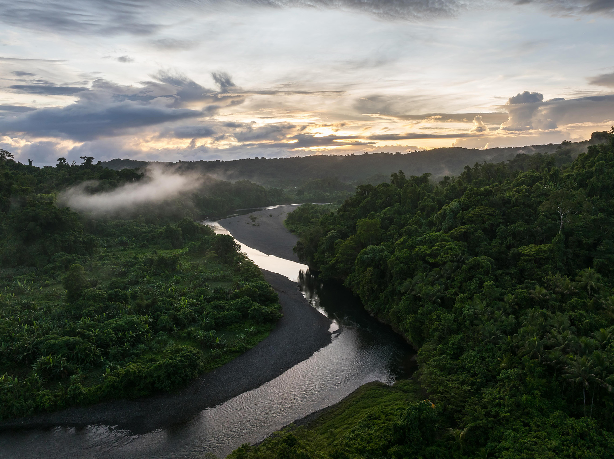 Drone view of Yato in the Solomon Islands shows a winding river amid lush jungles with fog and cloudy skies.