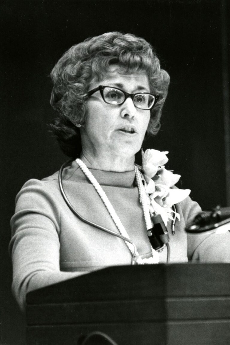 A woman in glasses, Loretta Ford, delivers a speech at a podium, showcasing her leadership as former dean of the School of Nursing.