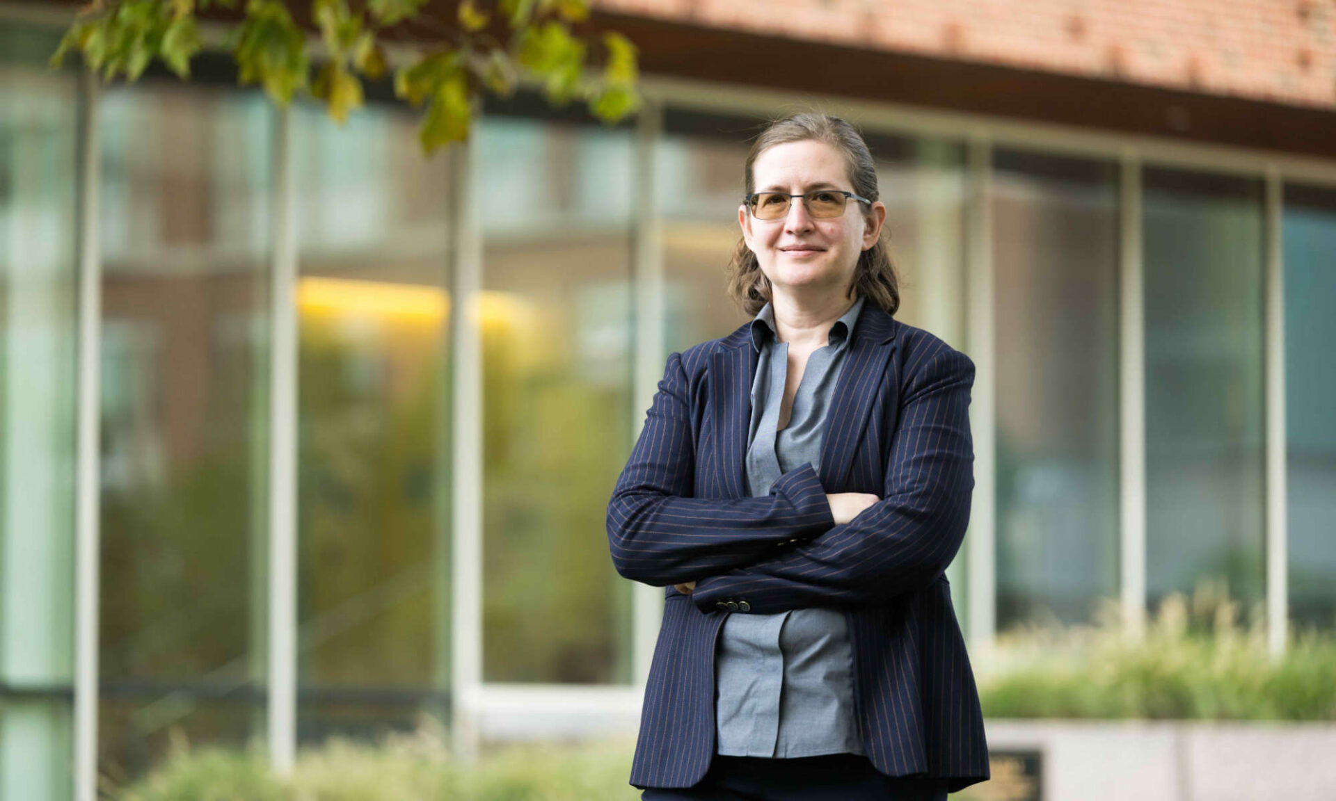 Amanda Stent smiles with their arms crossed in front of Wegmans Hall at the University of Rochester.