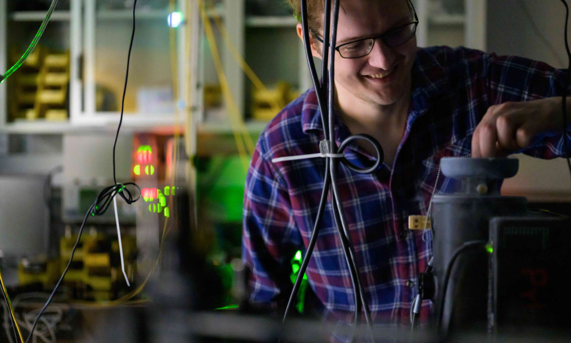 University of Rochester graduate student smiles while manipulating the apparatus in an optics lab.