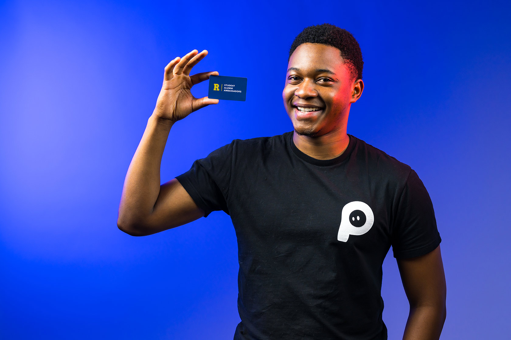 Tamuda Chimhanda holds up a business card with the Rochester Alumni Ambassadors logo on it.