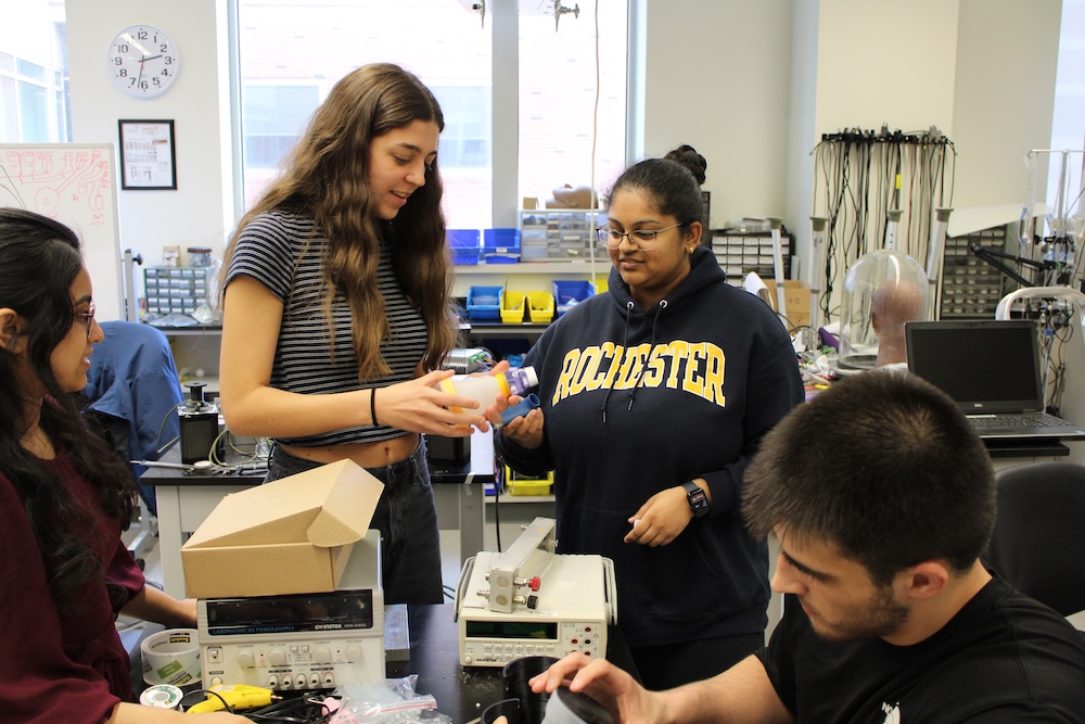 a group of four students work gather around a collapsible spacer for inhalers the team created.