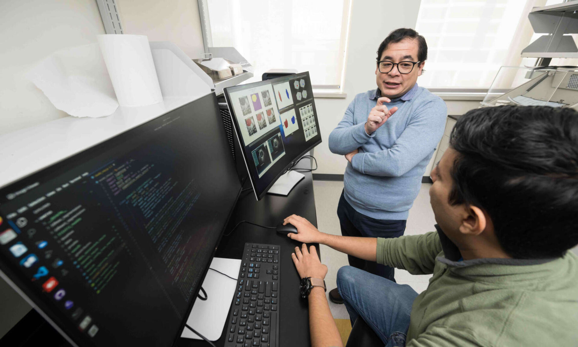 Benjamin Castañeda and Emilio Ochoa converse while reviewing data displayed on multiple computer screens.