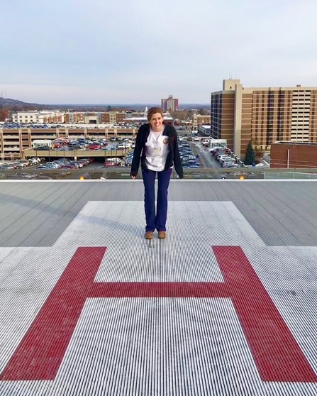 Farrell Cooke stands in front of the large red H of the helipad on the rooftop of Strong Memorial Hospital.