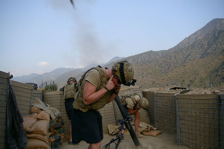 A US soldier plugs his ears as a rocket is launched behind him and other soldiers.