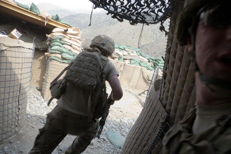 US army soldier seen from behind running into a shanty-like, outdoor space.