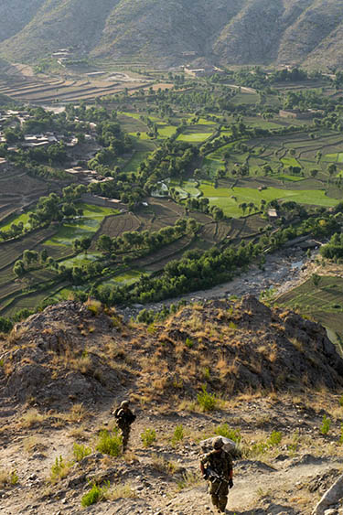 Two US soldiers in uniform seen from behind walking down into a valley in Afghanistan.