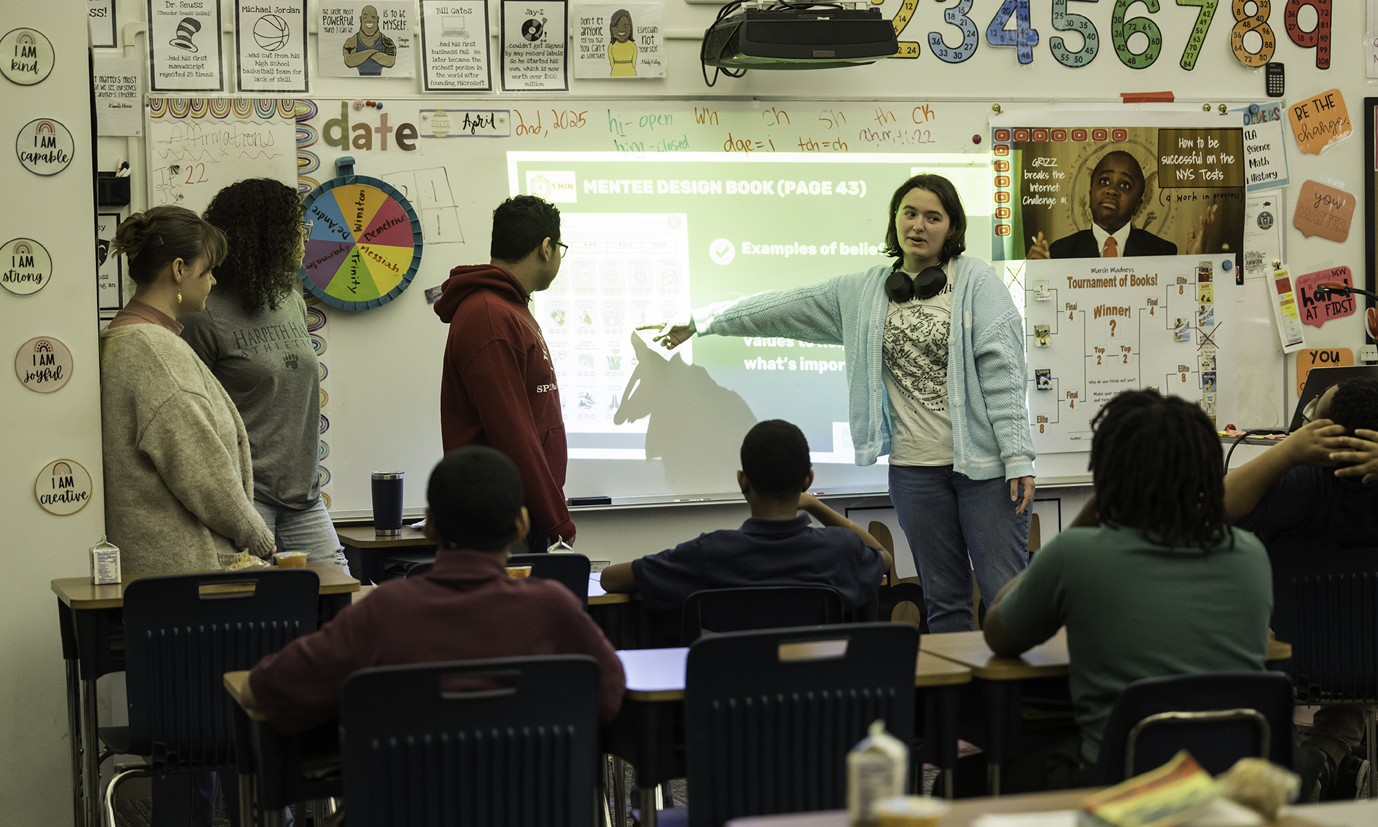 University of Rochester students lead a classroom activity using a projected “Mentee Design Book” while middle school students watch and participate.
