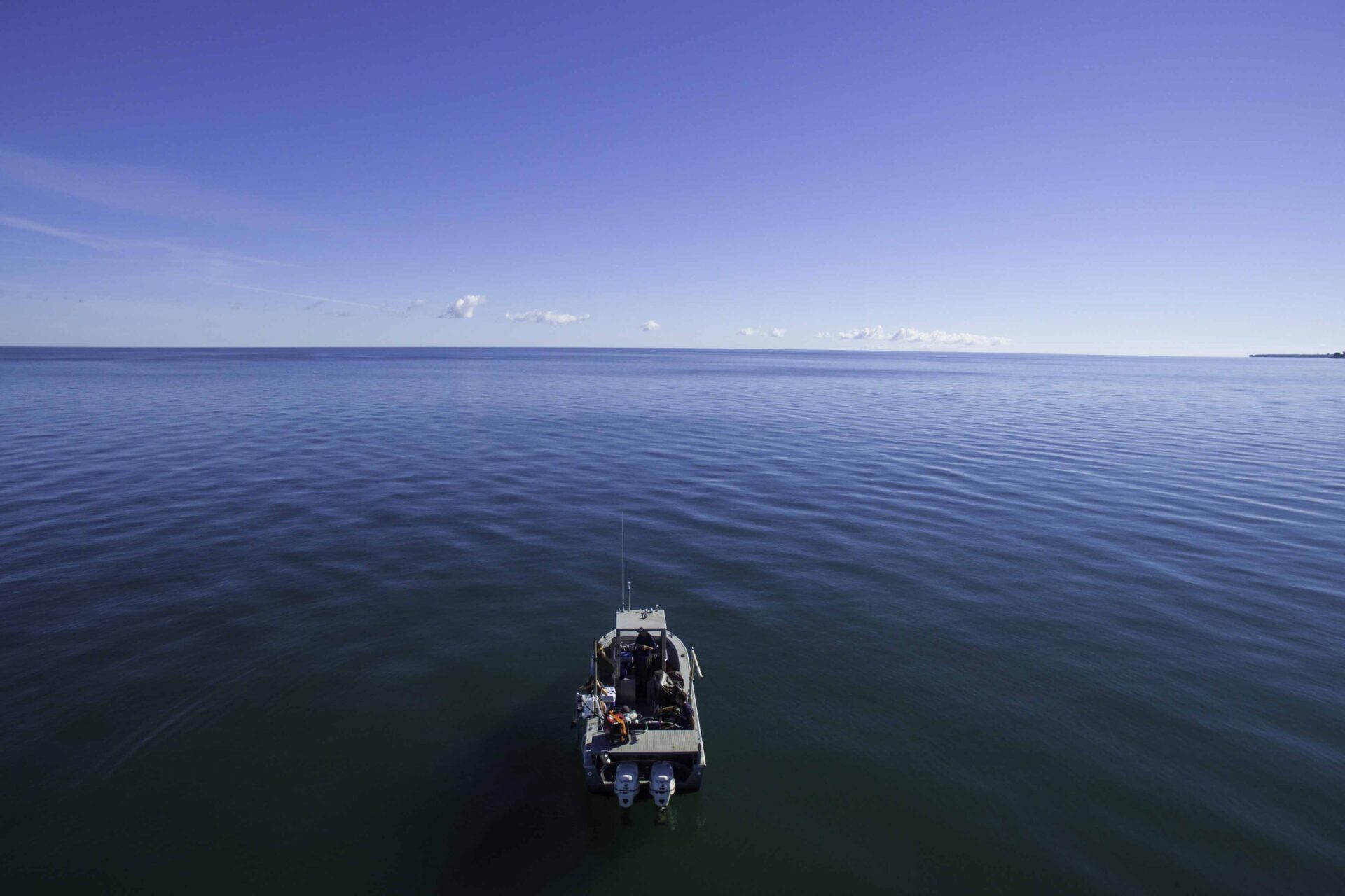 A boat seen from behind sailing off into Lake Ontario, which meets the horizon of the blue sky in the distance.
