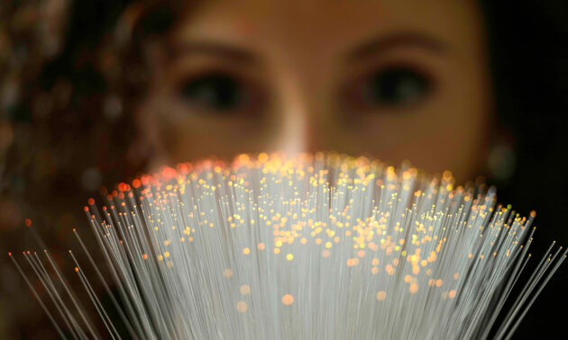 Close up of fiber optics cables lit up with a woman out of focusing behind them looking at the cables.
