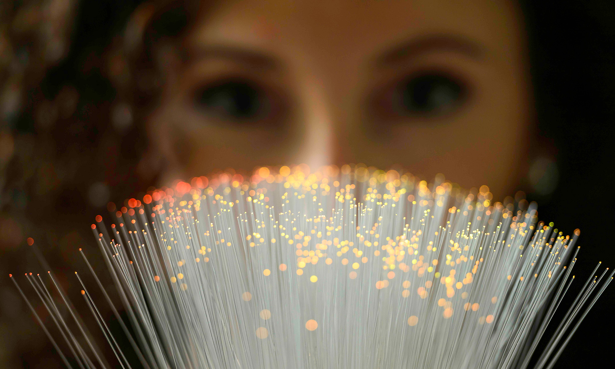Close up of fiber optics cables lit up with a woman out of focusing behind them looking at the cables.