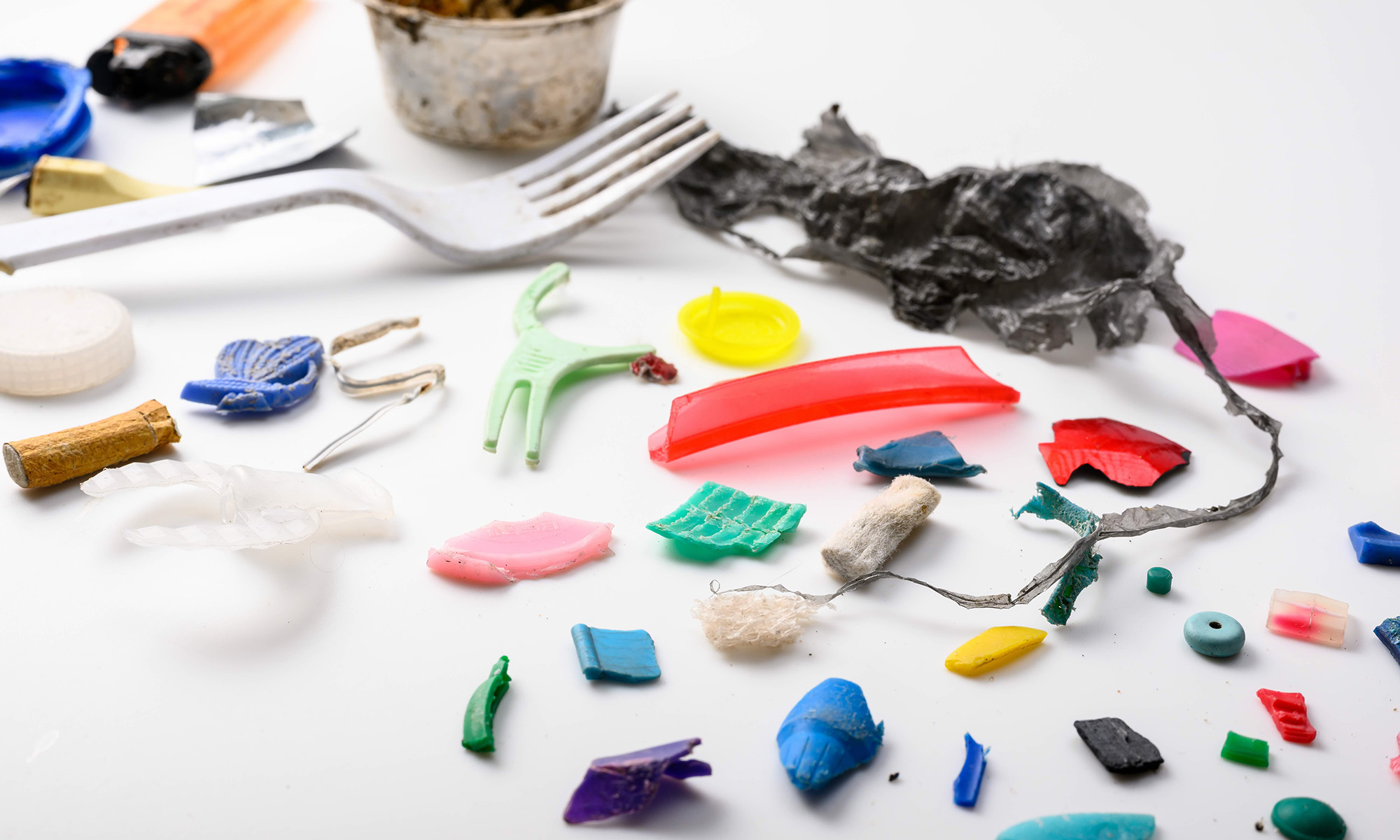 An array of plastics and microplastics, from utensils to cigarette butts, against a white background.