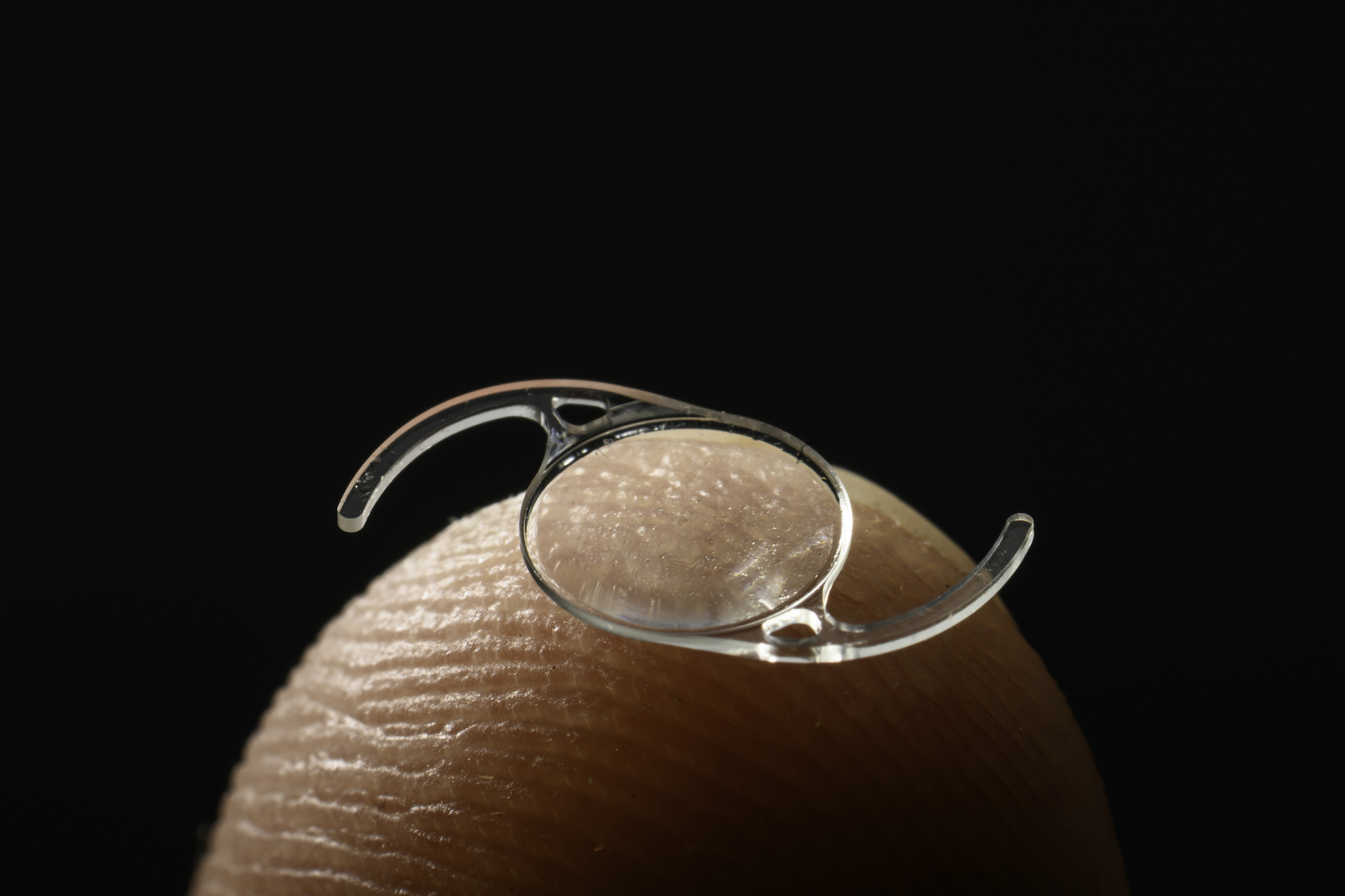 Intraocular lens photographed on a fingertip to show scale.