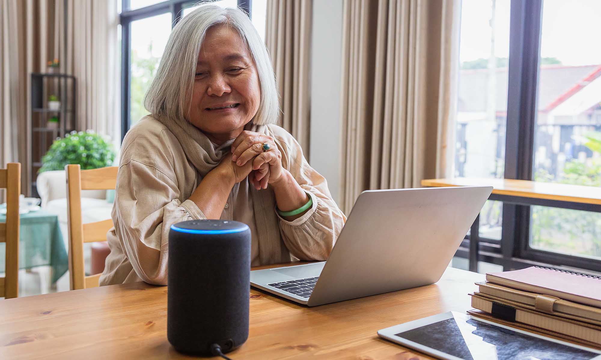 Asian senior women working with laptop computer and using smart speakers while setting in living room at home.