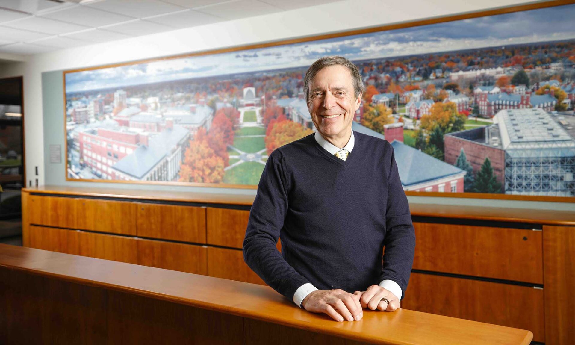 Doug Phillips smiles at the camera with a mural of the River Campus behind him.
