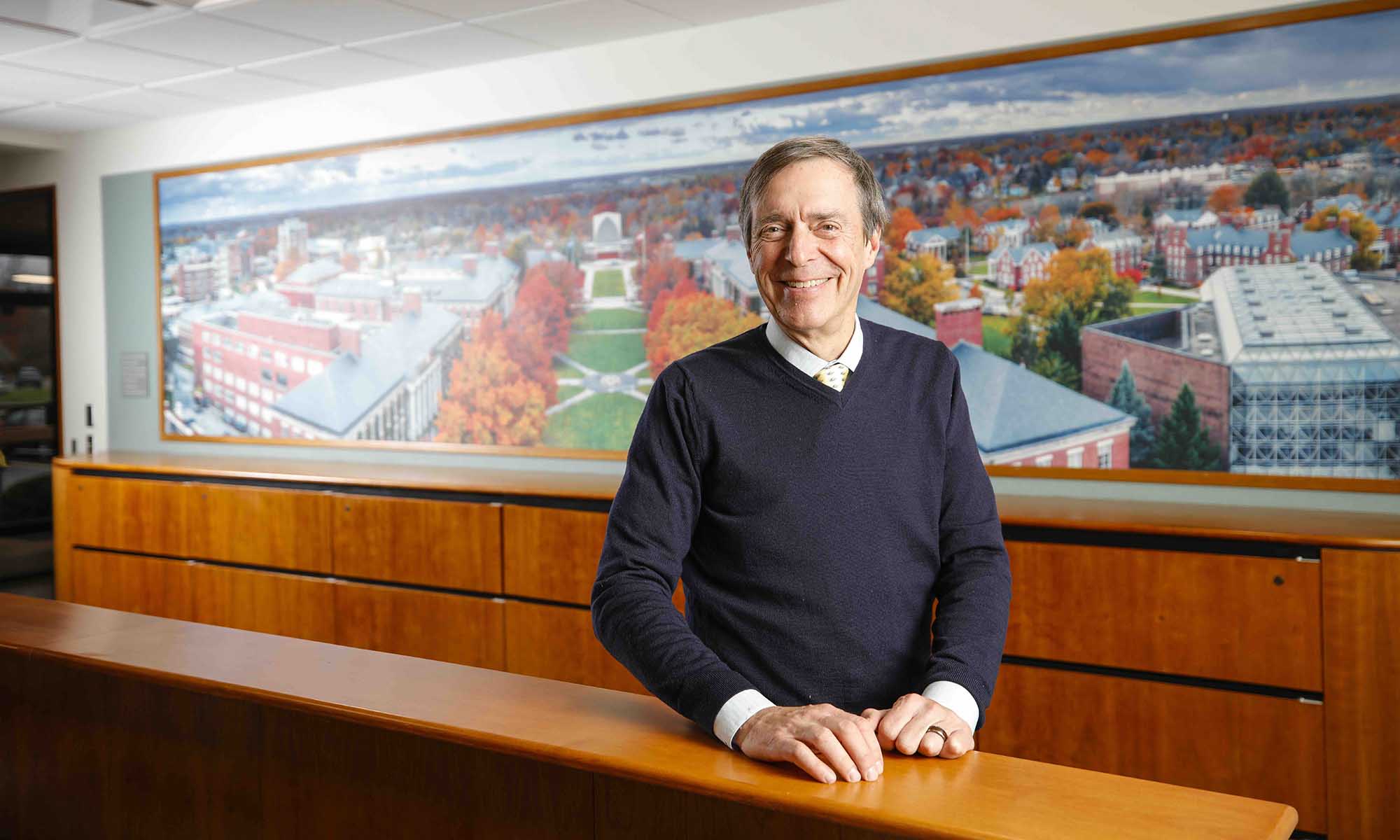 Doug Phillips smiles at the camera with a mural of the River Campus behind him.