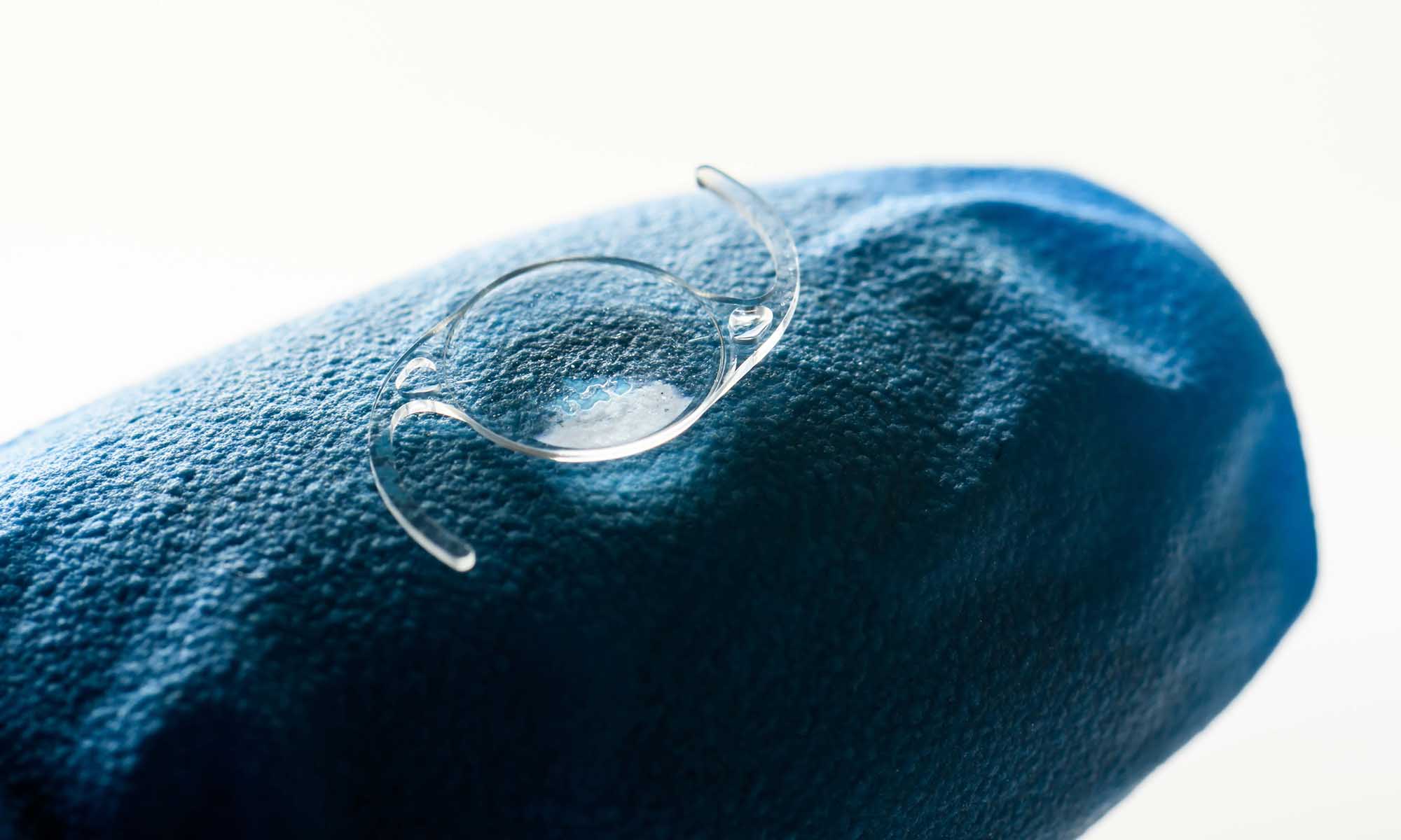 Close-up of a blue-gloved finger holding an intraocular lens.
