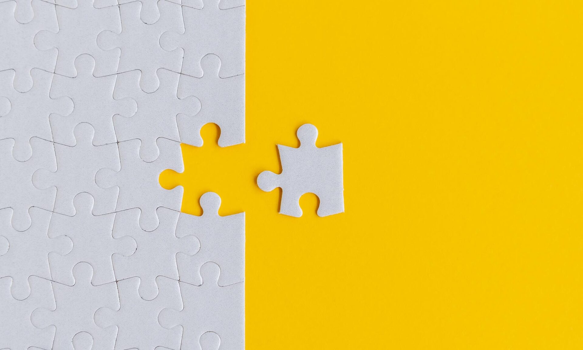 Image of a white puzzle against a yellow background with a final white piece just away from completing the puzzle.