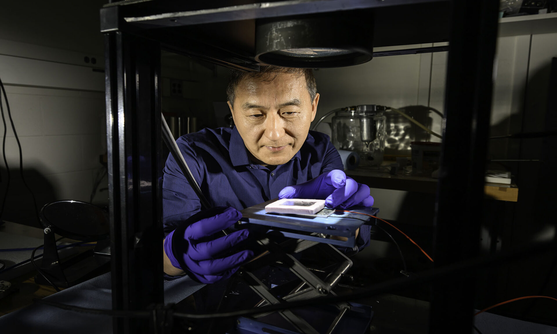 Chunlei Guo hovering over a simulator to test sunlight absorption of a solar thermoelectric generator device he holds.
