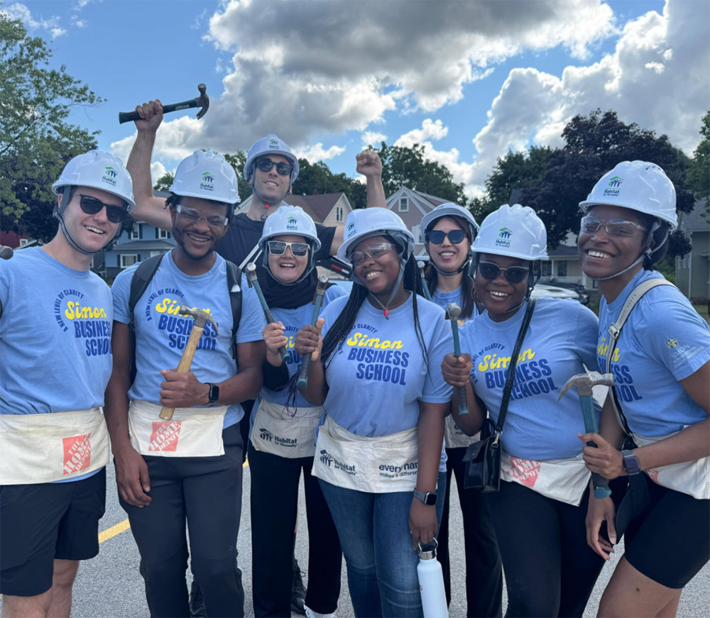 Group of Simon Business School MBA students smile for a photo after building the frame of a house.