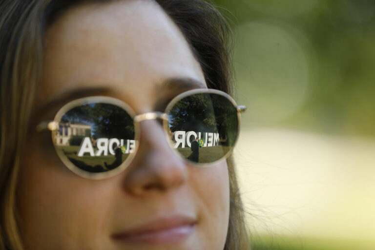 The Meliora letters reflected through sunglasses on a woman's face.