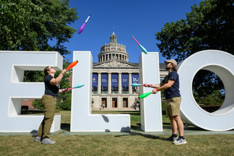 Jugglers perform in front of the Meliora letters.
