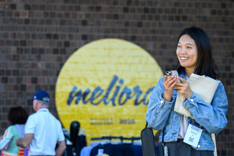 A person smiles in front of a Meliora sign in Meliora Village.