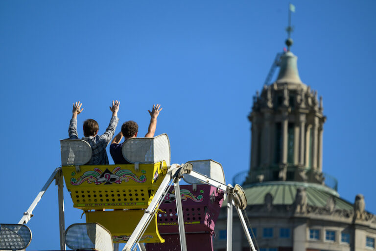 People with their arms up crest the top of a Ferris wheel ride.