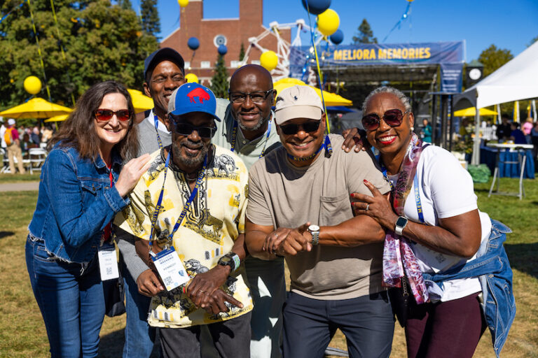A group of people pose together, smiling, in Meliora Village.