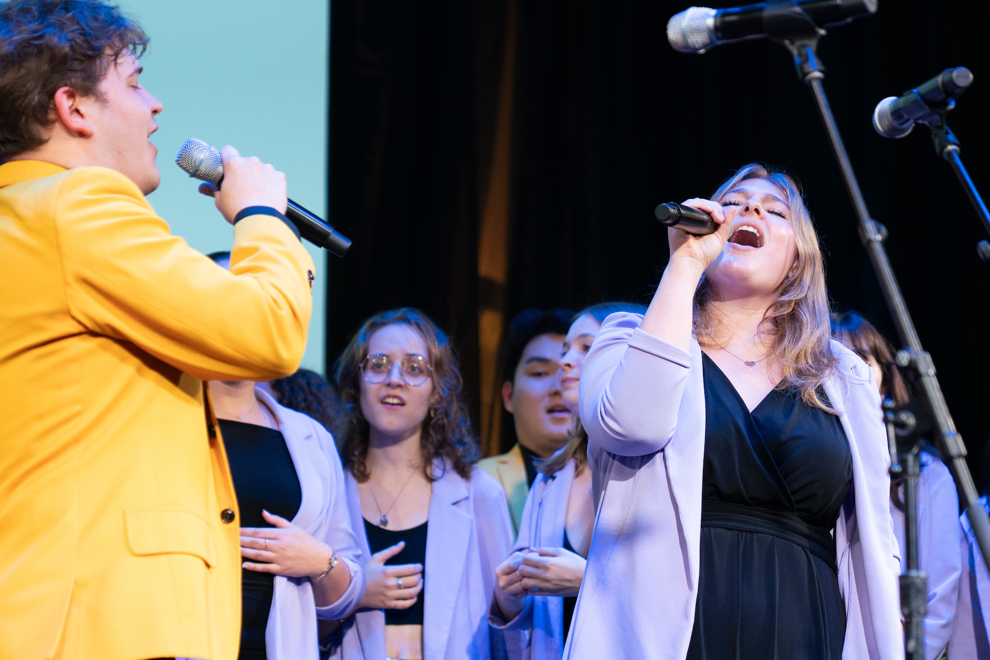 Members of a cappella groups Vocal Point and the Yellowjackets perform together on stage.